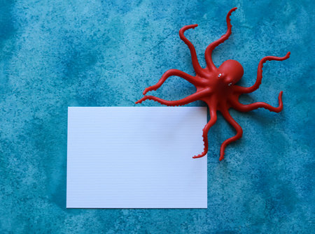 blank paper card with a toy octopus on a blue watercolor backgroundの写真素材