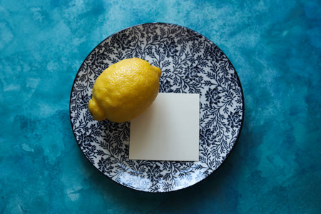a still life with a plate with a floral pattern and a bright yellow lemon on a blue watercolor backgroundの写真素材