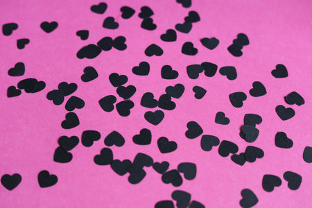 black heart shaped paper confetti on a pink paper backgroundの写真素材