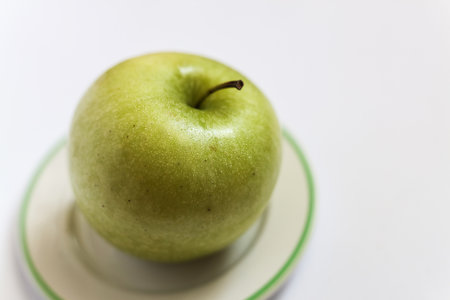 a single green apple covered in water drops on a small white plate against a white backgroundの写真素材