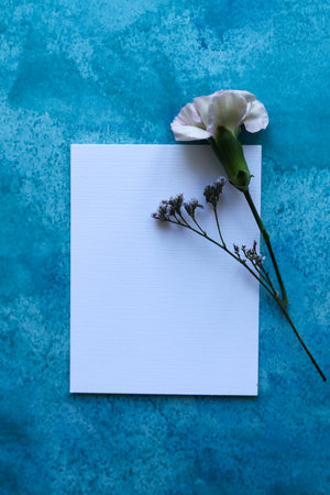 Blank card and flowers on blue background. Copy space for text.