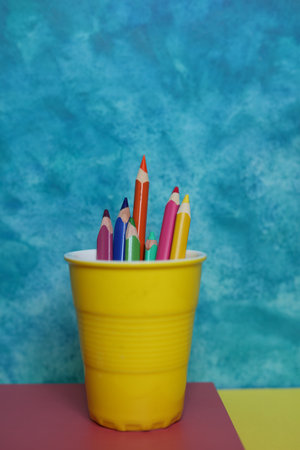 Colored pencils in a yellow pot on a blue background.