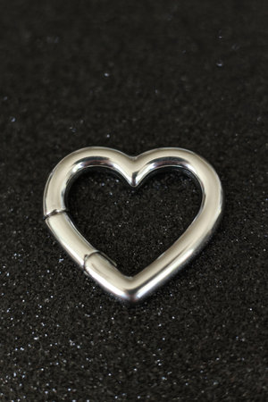 Silver heart-shaped earring on a black background. Macro photo.