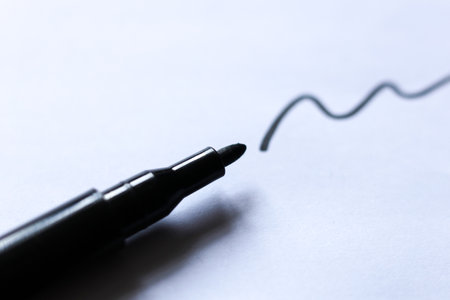 Close up of a black marker pen creating a wavy line on white paper. Minimal creative concept symbolizing art, writing, or design process in modern workspace.の写真素材