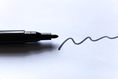 Close up of a black marker pen creating a wavy line on white paper. Minimal creative concept symbolizing art, writing, or design process in modern workspace.の写真素材