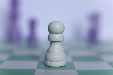 Close-up of a white chess pawn on a mint green chessboard with blurred purple pieces in the background. Minimalistic macro photographyの写真素材