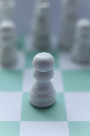 Close-up of a white chess pawn on a mint green chessboard with blurred purple pieces in the background. Minimalistic macro photographyの写真素材