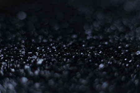 Abstract macro photograph of a black glitter surface with dramatic bokeh lights. Dark sparkling texture, soft blur, shimmering highlights and deep shadow tonesの写真素材