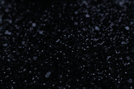 Abstract macro photograph of a black glitter surface with dramatic bokeh lights. Dark sparkling texture, soft blur, shimmering highlights and deep shadow tonesの写真素材