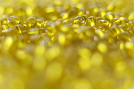 Close-up macro photograph of vibrant yellow transparent seed beads with a shallow depth of field. The image features glossy texture, sparkling reflections, soft bokeh backgroundの写真素材