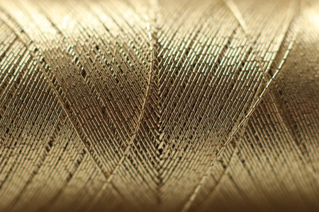 Macro close-up of a spool of golden thread showing detailed woven fibers and layered texture. The image highlights metallic sheen, craftsmanship, textile material,の写真素材