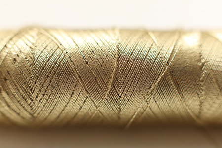 Macro close-up of a spool of golden thread showing detailed woven fibers and layered texture. The image highlights metallic sheen, craftsmanship, textile material,の写真素材