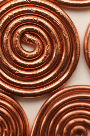 Close-up macro photograph of handcrafted copper spiral coils isolated on white background. Detailed view of metallic texture, warm copper tones, and circular geometric pattern.の写真素材