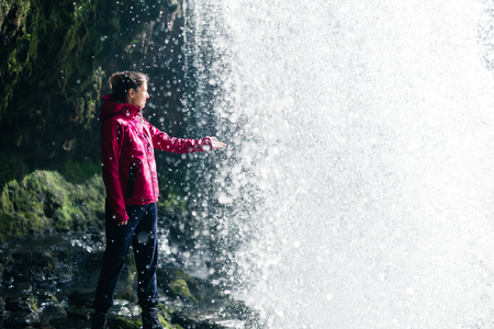 Feamale hiker, tourist, model touching water under the Sgwd Yr Eira Waterfall in Walesの写真素材