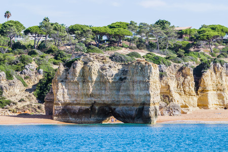 Cave and limestone arch formation. People walking crossing under the arch on the beach. Albufeira area, Algarve Portugal.の写真素材