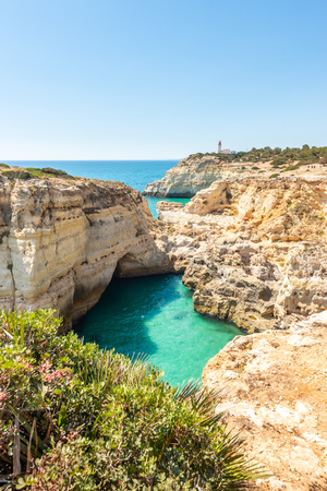 View of grotto cave, turquoise lagoon, limestone cliffs and lighthouse by the coasts of Algarve, Portugal, Europe.の写真素材