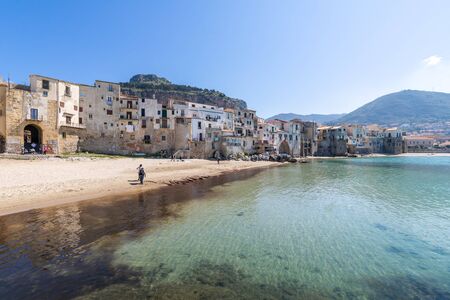 Idyllic view of turquoise sea and houses with Rocca di Cefalu rocky mountain in the background seen from historical old port of Cefalu - Sicily, Italyの写真素材