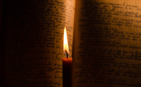 Burning candle on an open book in dark room with copy space. Hands of a man reading a holy bible with a lit candleの写真素材