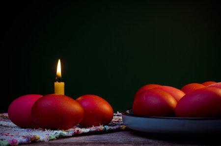 Easter eggs and lit candle on a wooden table. Dark background.の写真素材