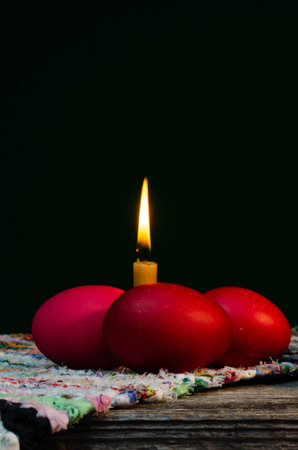 Easter eggs and candle on old wooden table, black background.の写真素材