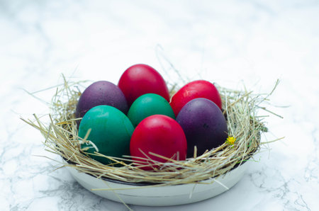 Colorful easter eggs in a basket on a white marble backgroundの写真素材