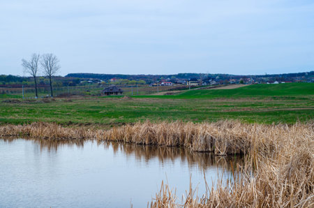Spring landscape with a small river and the village in the background.の写真素材