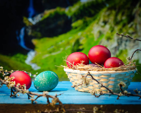Colorful easter eggs in a basket on the background of a beautiful waterfallの写真素材