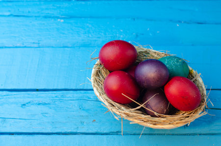 Colorful easter eggs in a basket on a blue wooden backgroundの写真素材