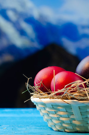 Easter eggs in a basket on a blue wooden table with mountains in the backgroundの写真素材