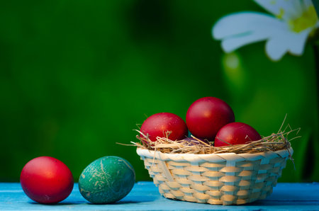 Easter eggs in a basket on a wooden table on a green backgroundの写真素材