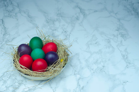 Colorful easter eggs in a basket on a white marble backgroundの写真素材