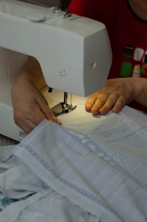 Sewing machine and woman hands working on white fabric, close upの写真素材