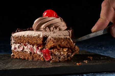 fork eating slice of chocolate cake with cherries