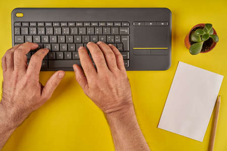 hand typing on keyboard, with paper to put your own note on yellow backgroundの写真素材
