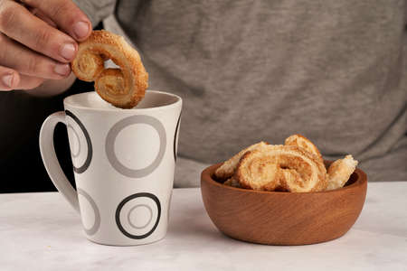 man's hands dipping puff pastry palmeritas orejitas cup tea coffeeの写真素材