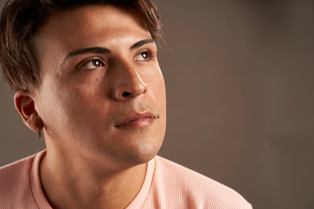 close up latin man looking up isolated on gray background with pink clothing copy spaceの写真素材
