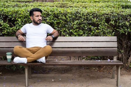 latin man sitting cross-legged on plaza benchの写真素材