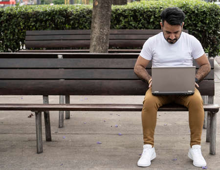 Latin man using his laptop on a plaza benchの写真素材