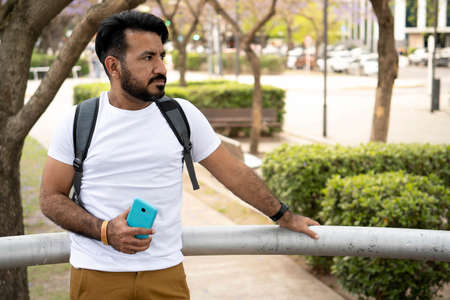 latin man with beard leaning on a railing in an urban environment looking at his cell phoneの写真素材