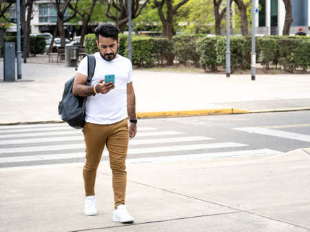 Latin man with beard walking in urban environment looking at his cell phoneの写真素材