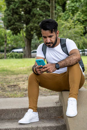 latino man sitting on the stairs of a park using his cell phoneの写真素材