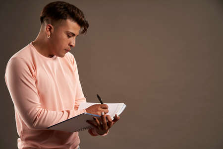 latin man writing in notebook standing facing downの写真素材