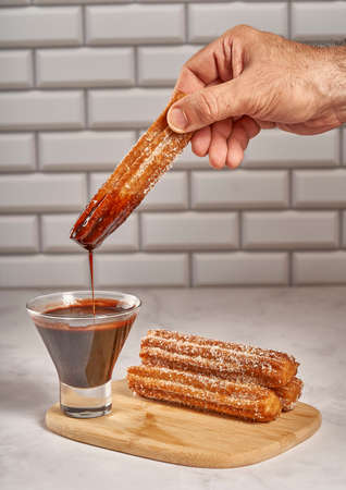 Dipping churro in chocolate sauce. Wooden board with churrosの写真素材