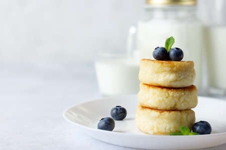 Cottage cheese pancakes, syrniki, curd fritters with fresh blueberries and milk on light background....