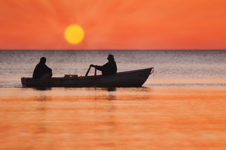 Two silhouettes of men in a fishing boat at sunsetの写真素材