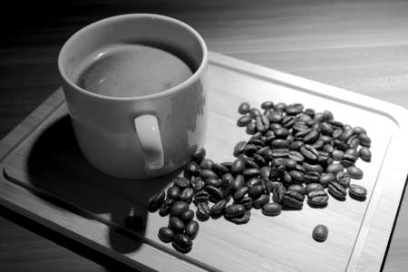 A cup of coffee with coffee beans on a bamboo board. Black and white photography.
