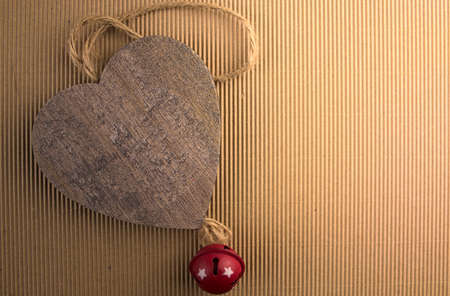 Wooden heart with a red metal bell on a corrugated cardboard background.の写真素材