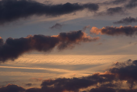 The sky with dark blue clouds illuminated by warm orange light of the setting sun.の写真素材