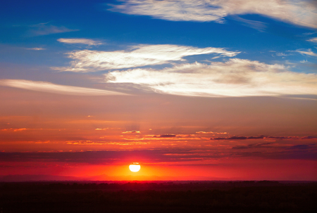 Dramatic sunset with gradient toned evening sky, sun and spindrift cloudsの写真素材