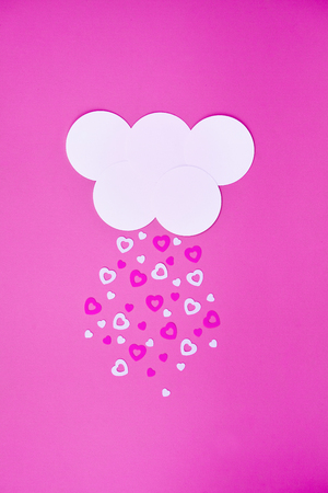 White cloud on pink background with pink and white hearts falling down like snow or rain. Trendy simple paper cut Valentines day, wedding, charity concept for invitations, greeting cards, postersの写真素材